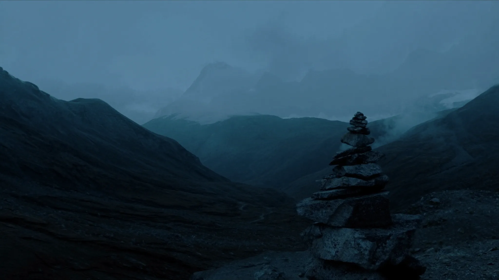 Un cairn de pierres empilées, repère de crête, se détache dans la lumière bleutée de l'aube sur un paysage alpin suisse brumeux.